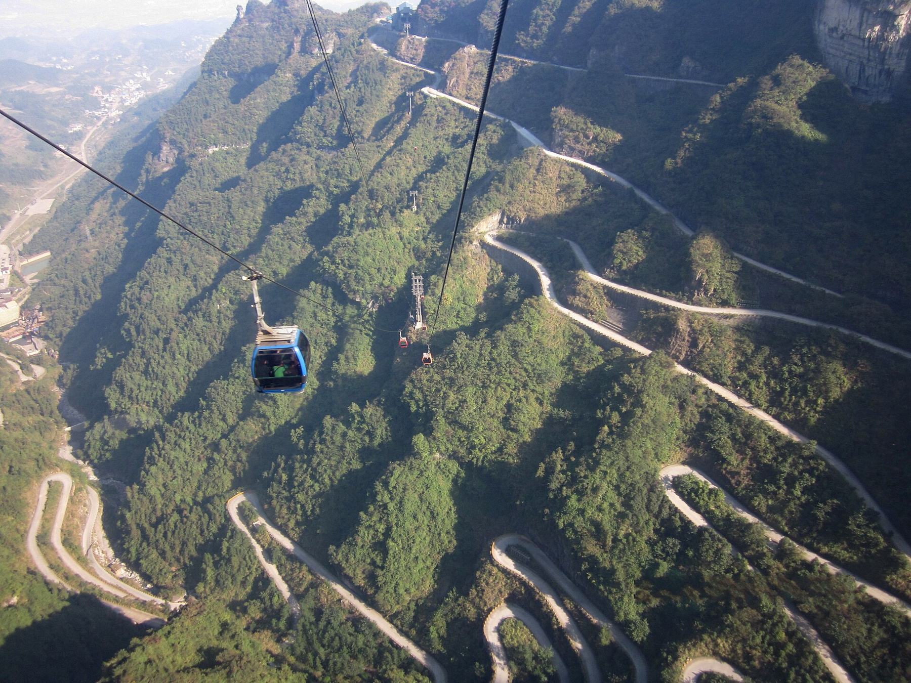 Teleférico de la Montaña Tianmen sobre la carretera de curvas y los picos boscosos de Zhangjiajie